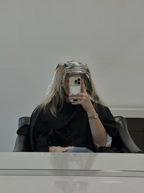 Girl holding phone in front of mirror with foils in her hair