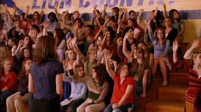 Scene from Mean Girls where teenagers are raising their hands in gymnasium